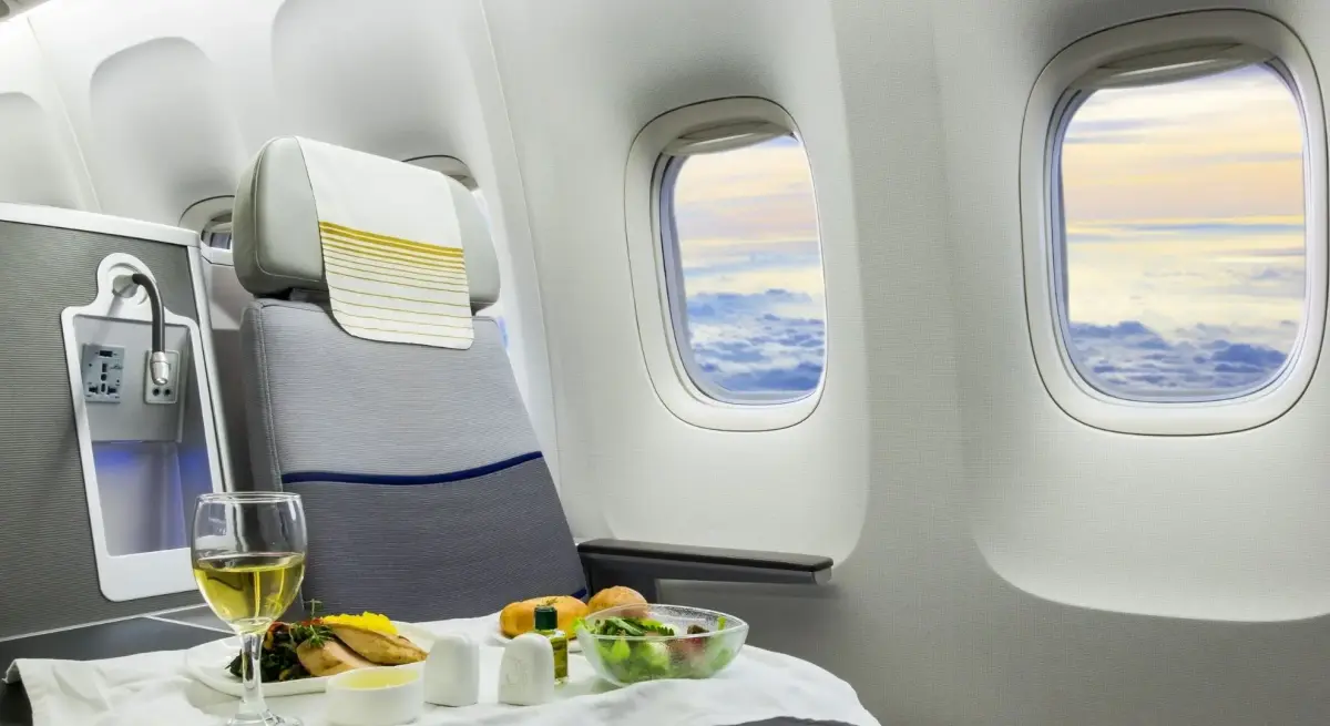 Business class interior with meal service beside a leather seat overlooking clouds at sunset