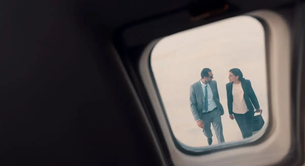 Two business travellers walking across a private jet tarmac in Indonesia, viewed through the aircraft cabin window