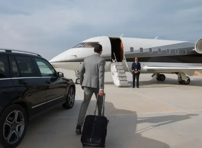 Business executive with luggage walking toward a private jet on the tarmac, greeted by crew, for a corporate charter flight
