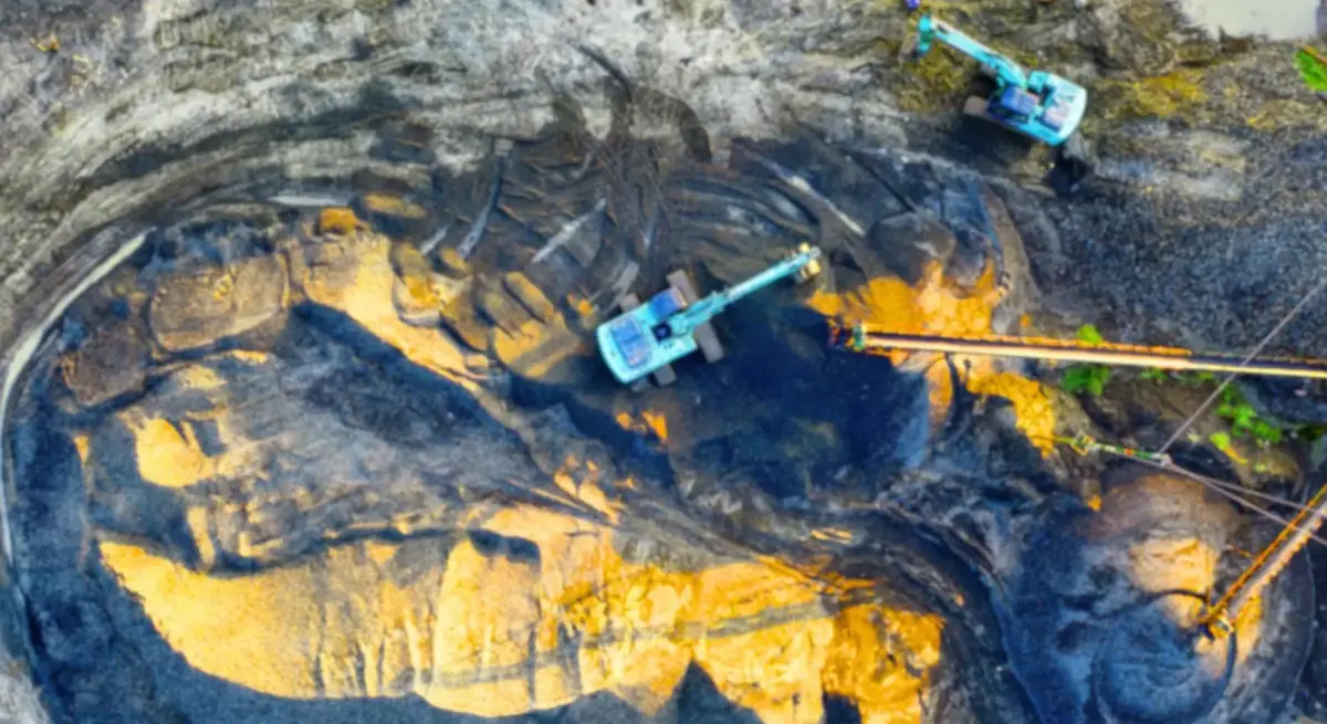 Aerial view of an open-pit mining site in Indonesia with excavators and conveyor belt operating across mineral-rich terrain