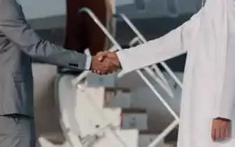 Business traveler in suit shaking hands with client in traditional white thobe on the tarmac beside a private jet in Indonesia