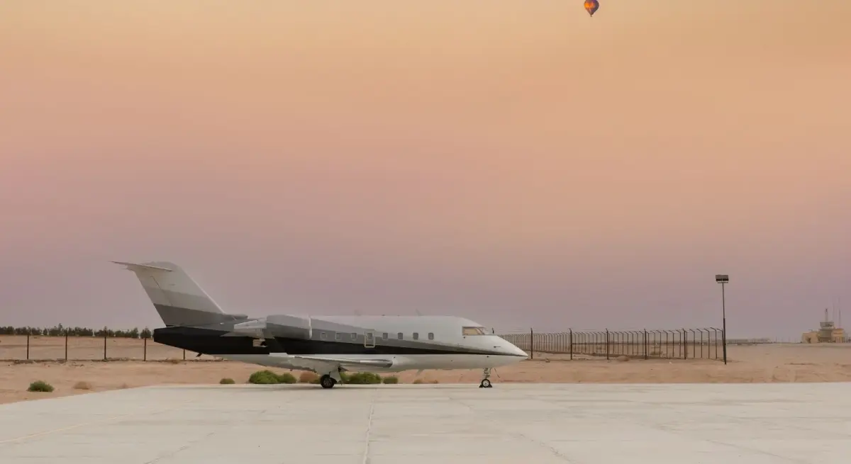 Private jet parked on a desert tarmac with hot air balloons, evoking luxury charter travel for exclusive destinations