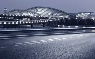 Shanghai Hongqiao Airport illuminated at dusk, showcasing its sweeping glass terminal and curved access road for private jet charter arrivals