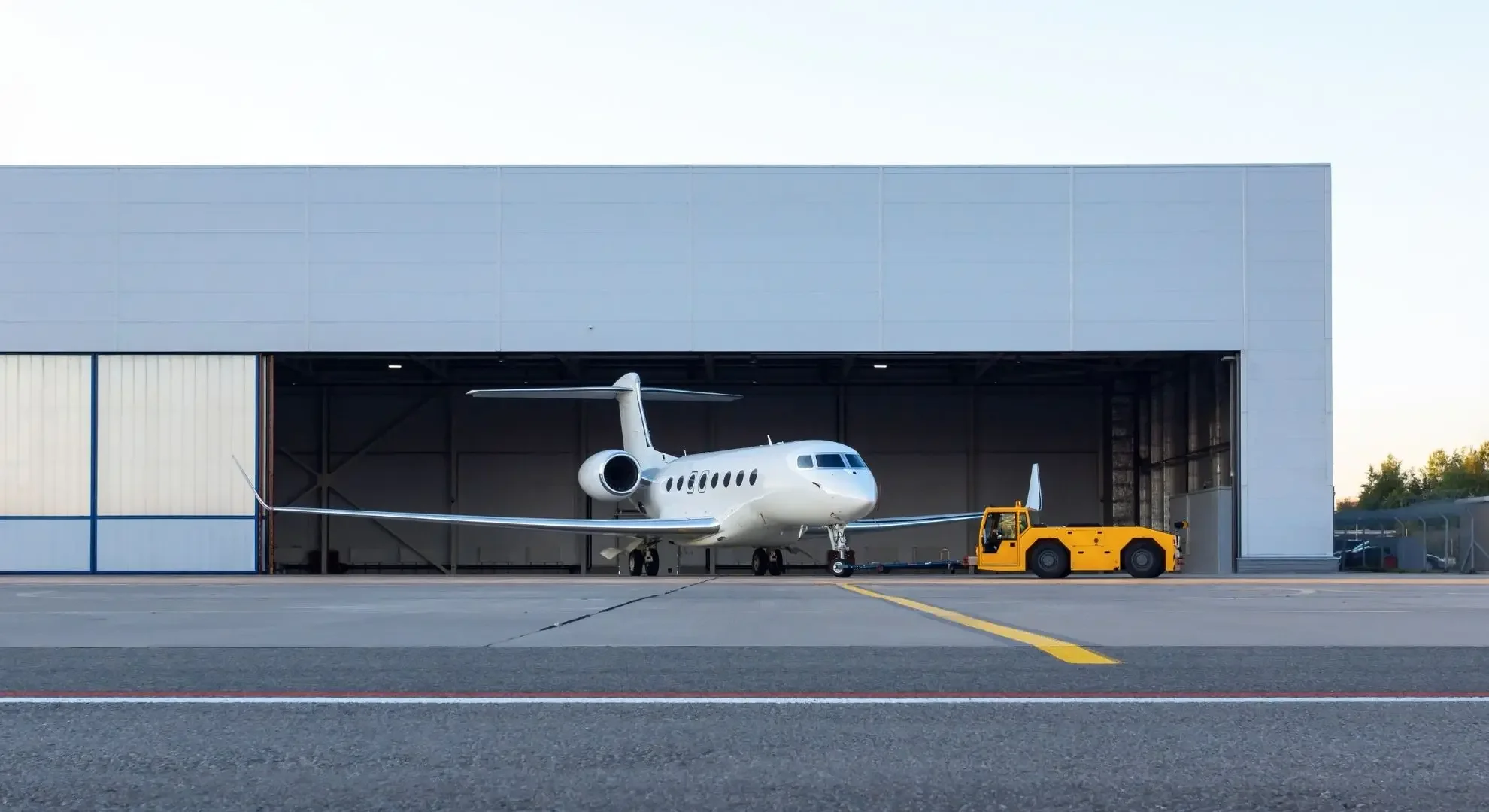 White private jet being towed out of an aviation hangar by a vehicle, ready for departure on a charter flight from Hong Kong
