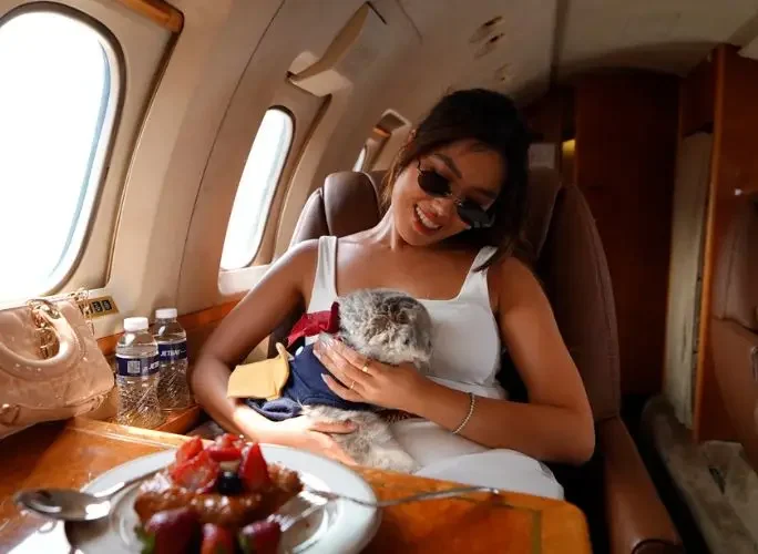 Smiling woman cradling a fluffy cat in a luxurious private jet cabin with fresh fruit and Jetbay water bottles, showcasing pet-friendly charter travel to Indonesia