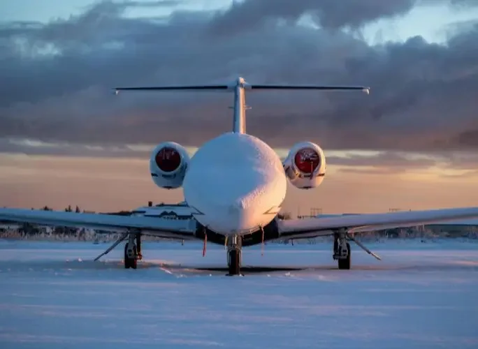 Private jet covered in snow at sunset on an airfield during the winter season