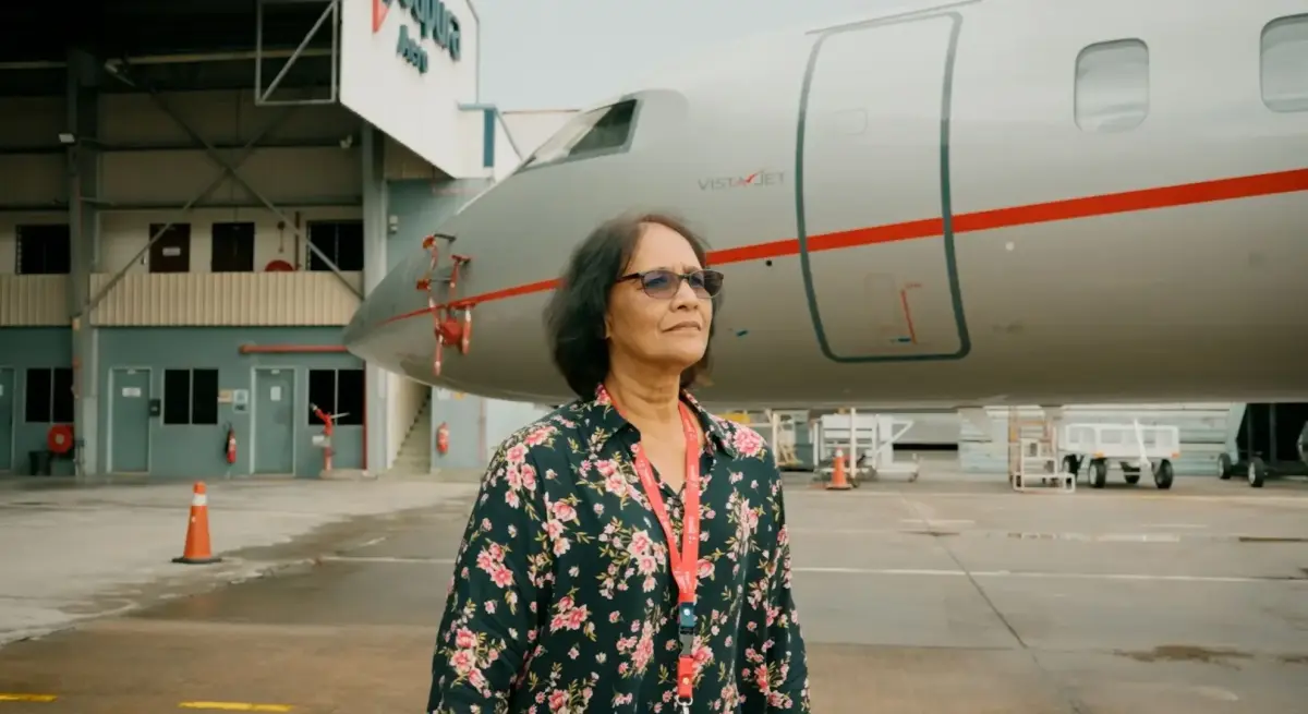Professional woman in floral attire standing confidently beside luxury private jet in modern hangar facility