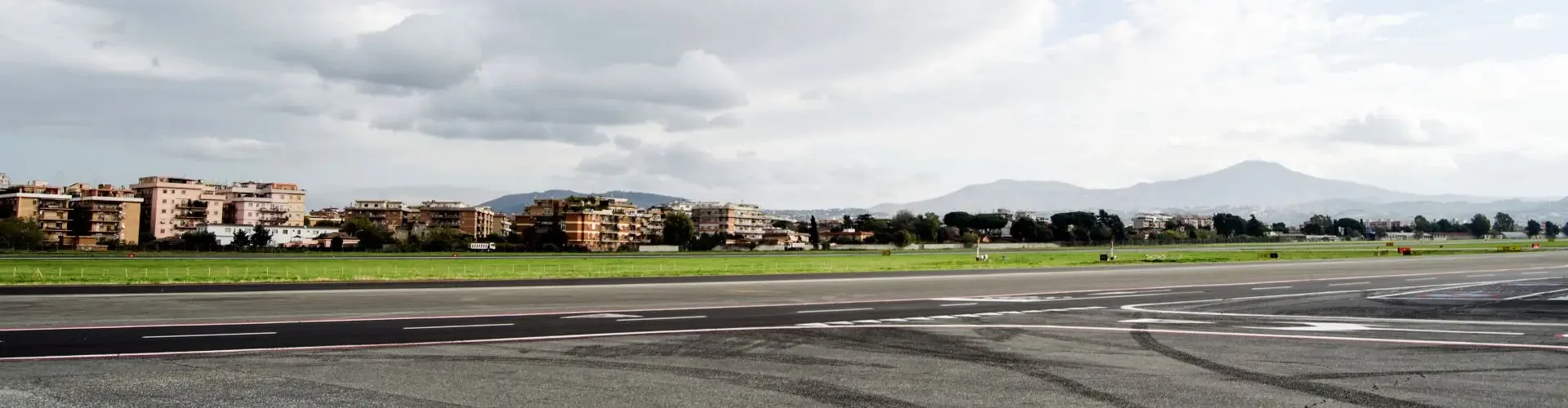 Private Jet Charter to Rome Ciampino Airport (CIA/LIRA) Open tarmac at Rome Ciampino Airport with a bird in flight over the runway, mountains and city skyline visible in the background