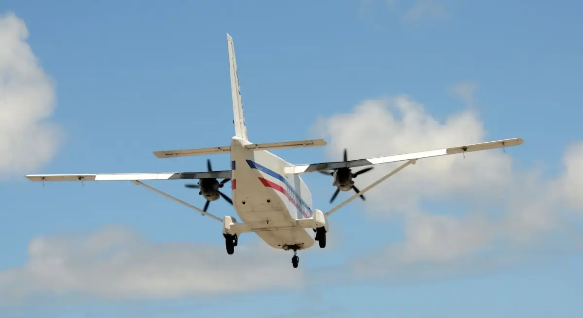 Twin-engine turboprop charter aircraft on approach to Batulicin Bersujud airport, viewed from below against a blue sky