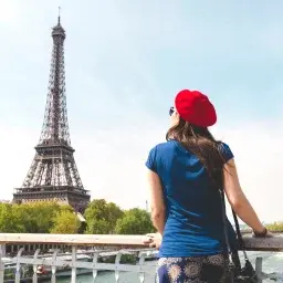 Woman in red beret admiring Eiffel Tower from Seine riverbank, representing luxury Paris destinations