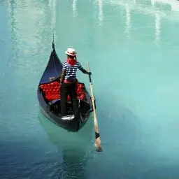 Venetian gondolier in striped shirt navigating traditional black gondola through turquoise canal waters