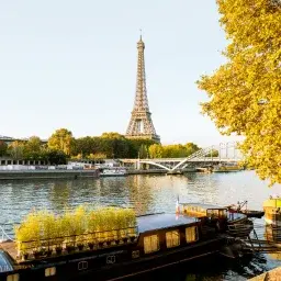Eiffel Tower rising above Seine River with golden autumn trees and traditional houseboats in Paris