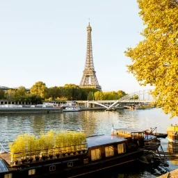 Eiffel Tower rising above Seine River with golden autumn trees and traditional houseboats in Paris