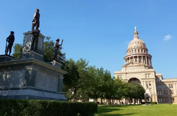 Texas State Capitol building with distinctive dome and monument on manicured grounds in Austin