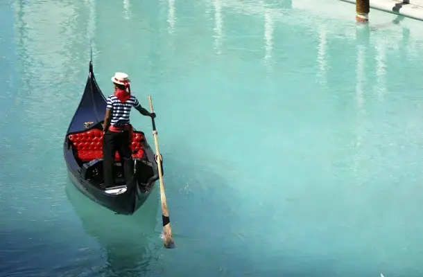 Gondolier in striped shirt navigating traditional black gondola through turquoise Venice canal waters