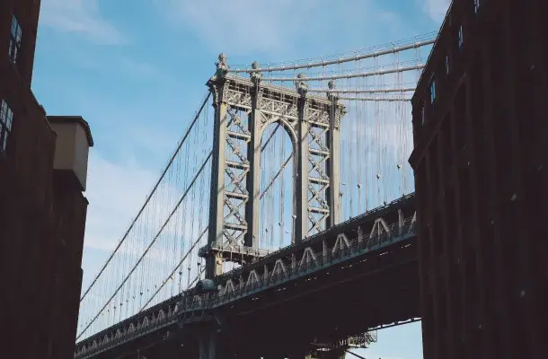 Manhattan Bridge spanning East River with iconic stone towers and suspension cables framed by buildings