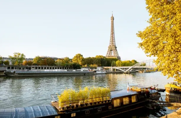 Eiffel Tower rising above Seine River with golden autumn trees and traditional houseboats in Paris
