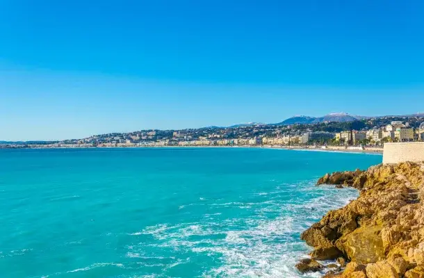 Stunning turquoise Mediterranean coastline of Nice with rocky cliffs, azure waters, and elegant French Riviera buildings under clear blue skies