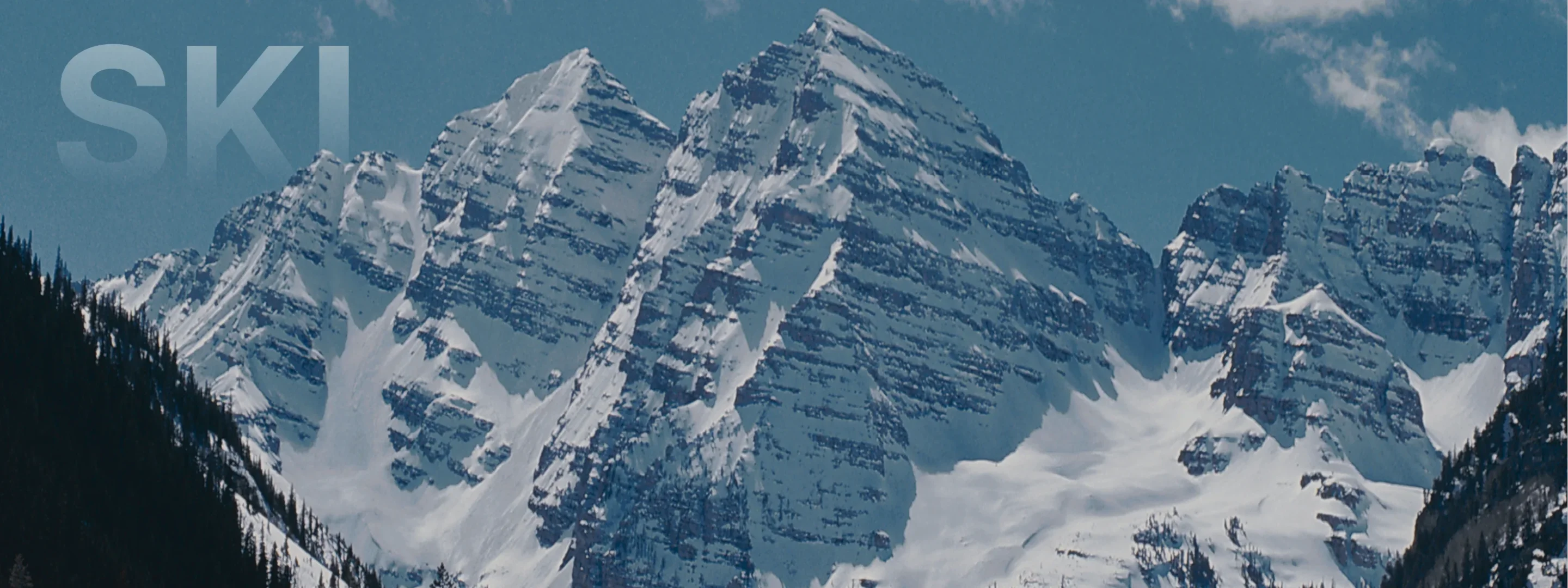 Snow-covered mountain peaks and evergreen forests create a dramatic alpine landscape in Aspen