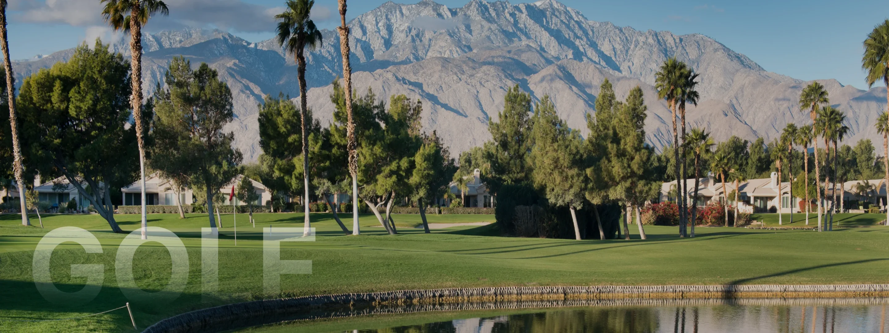 Pristine golf course with manicured greens and palm trees against dramatic snow-capped mountains in Palm Springs