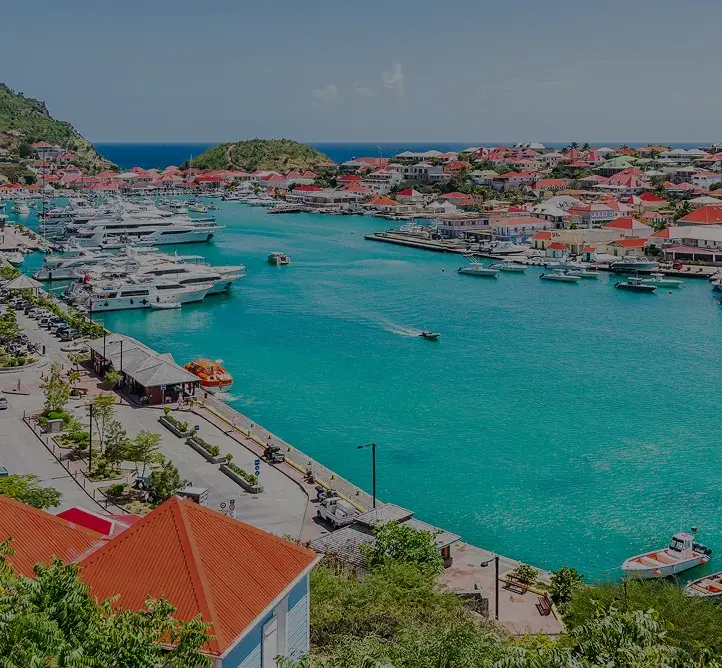Stunning aerial view of St. Barts harbor with luxury yachts, red-roofed villas, and turquoise waters