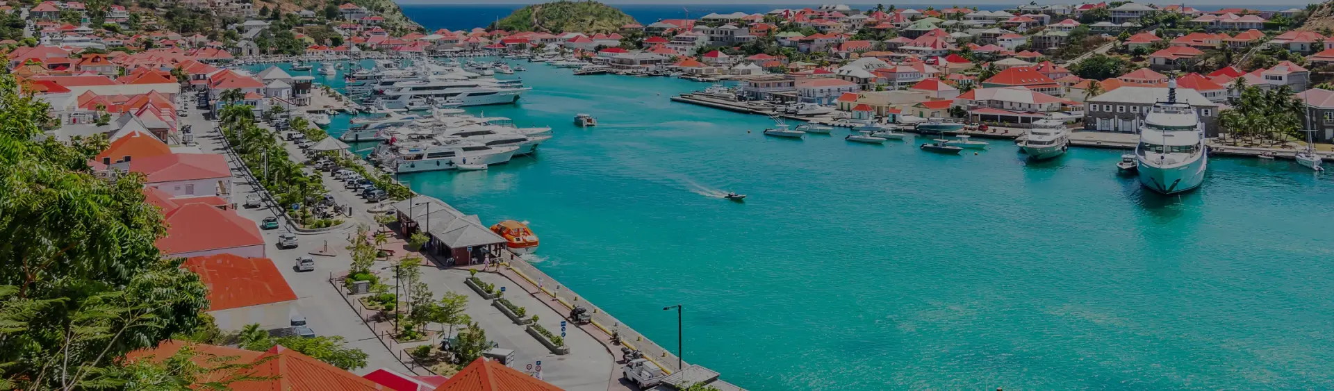 Stunning aerial view of St. Barts harbor with luxury yachts, red-roofed villas, and turquoise waters