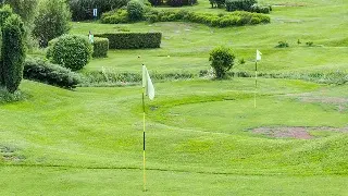 Pristine golf course with manicured greens, flagsticks, and rolling fairways surrounded by lush landscaping