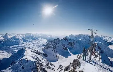 Snow-covered mountain peaks and ski slopes under bright blue sky with sun, showcasing alpine terrain