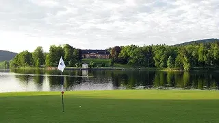 Pristine golf green with flag overlooking serene lake and forested hills at Pinehurst resort