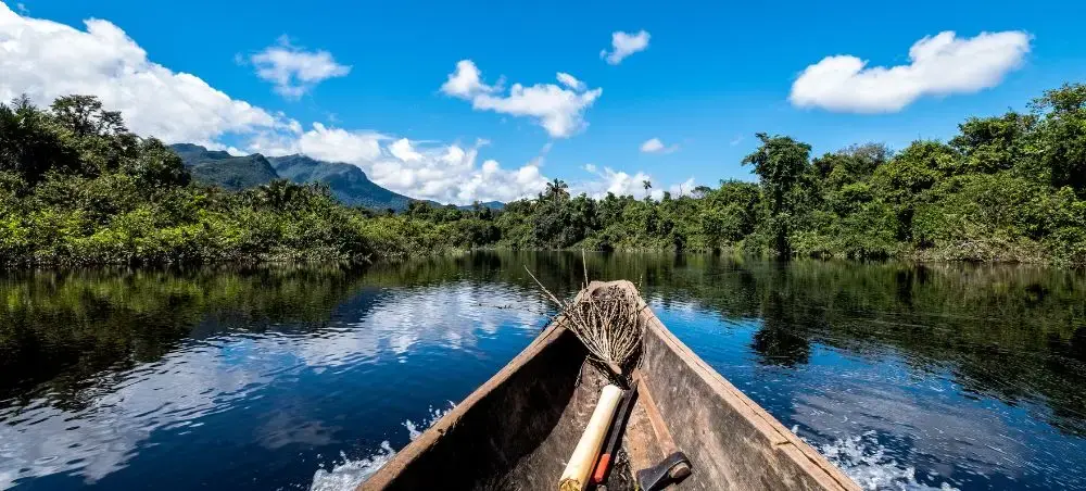 Traditional wooden canoe navigating pristine Amazon rainforest waters with lush jungle and mountains