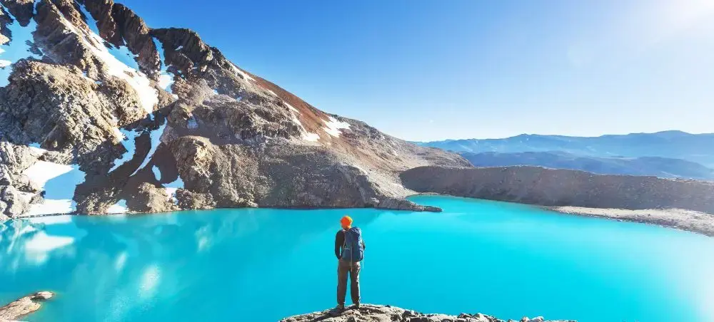 Hiker overlooking stunning turquoise crater lake surrounded by snow-capped Andes mountains in Argentina