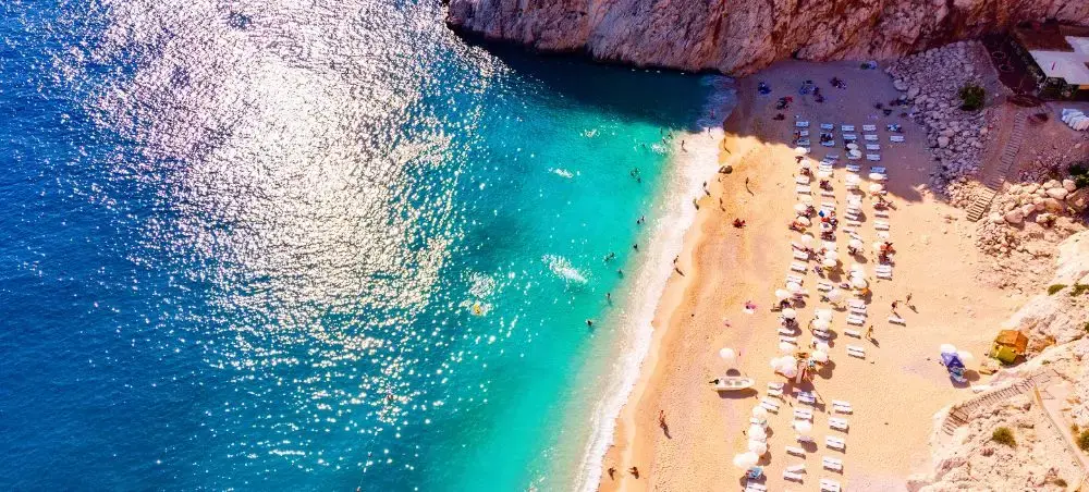 Aerial view of pristine turquoise waters meeting golden sand beach with sunbathers in Antalya, Turkey