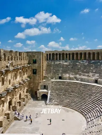 Ancient Roman amphitheater in Antalya with stone seating tiers and tourists exploring under blue sky