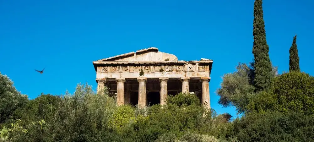 Ancient Greek temple with Doric columns nestled among Mediterranean trees under brilliant blue Athens sky