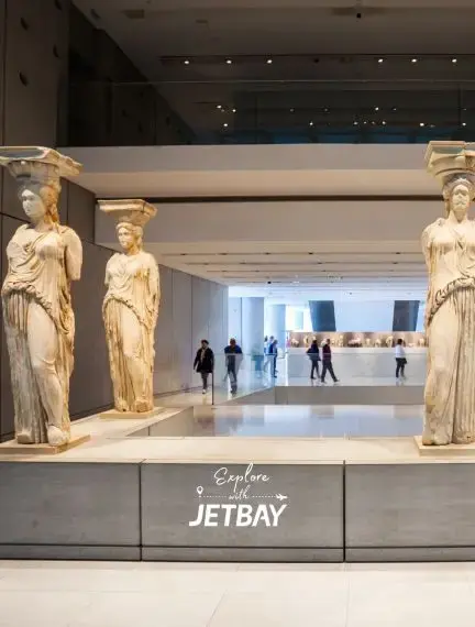 Ancient Greek caryatid statues displayed in modern Athens museum with visitors exploring cultural exhibits
