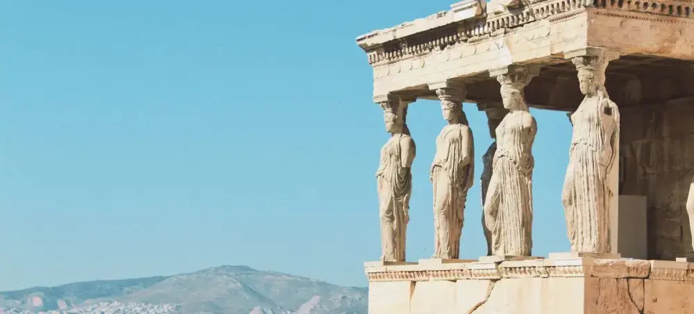Ancient Caryatid sculptures supporting the Erechtheion temple on Athens Acropolis against blue sky