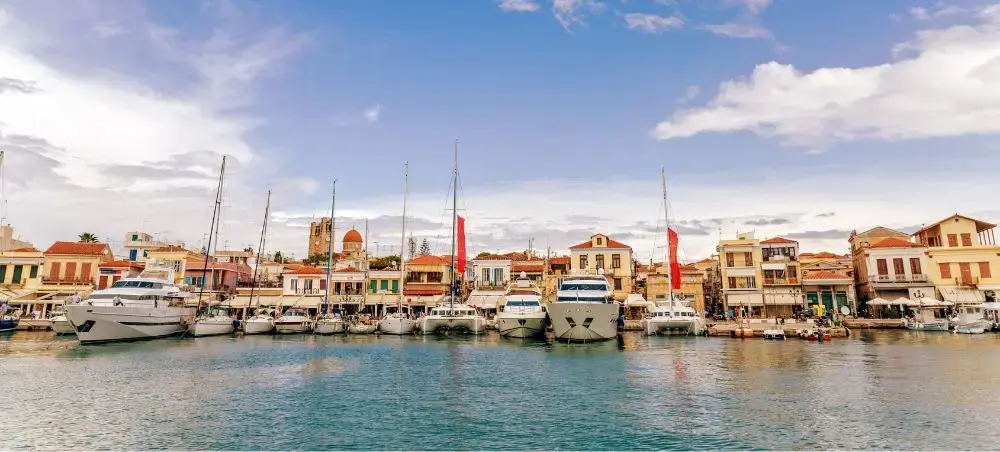 Luxury yachts and sailboats moored in a picturesque Greek harbor with traditional Mediterranean architecture