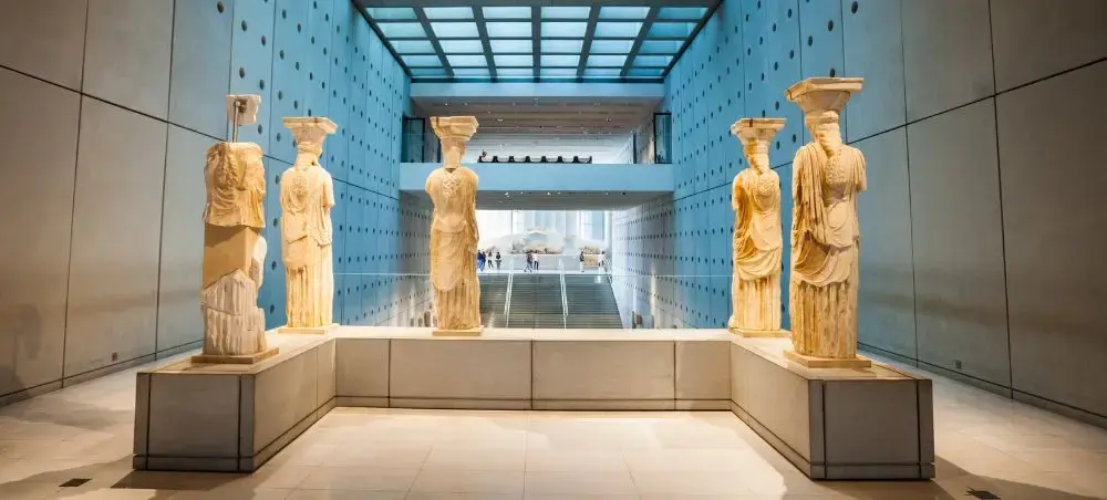 Ancient Greek statues displayed in modern Athens museum gallery with dramatic lighting and glass ceiling