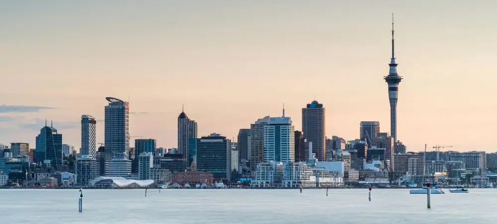 Auckland skyline featuring Sky Tower and modern skyscrapers reflected in harbor waters at golden hour
