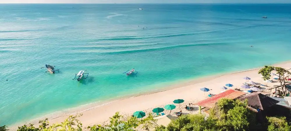 Pristine Bali beach with turquoise waters, traditional fishing boats, and luxury resort umbrellas on white sand