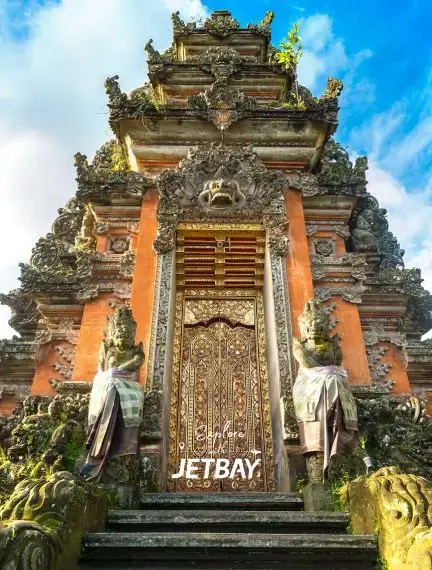 Ornate Balinese temple entrance with intricate stone carvings and golden doors under blue sky in Bali