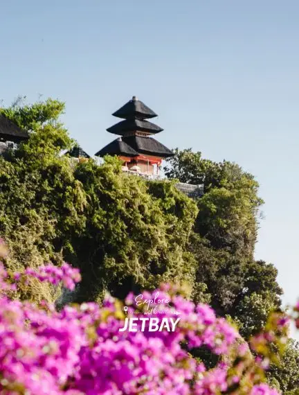 Traditional Balinese temple pagoda surrounded by lush tropical vegetation and vibrant pink flowers in Bali