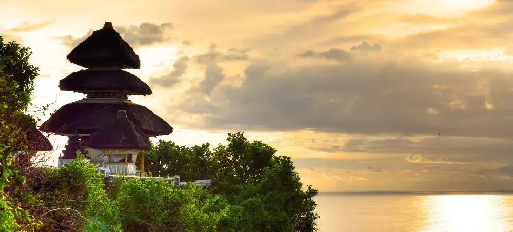Traditional Balinese temple overlooking serene ocean waters during golden sunset in Indonesia