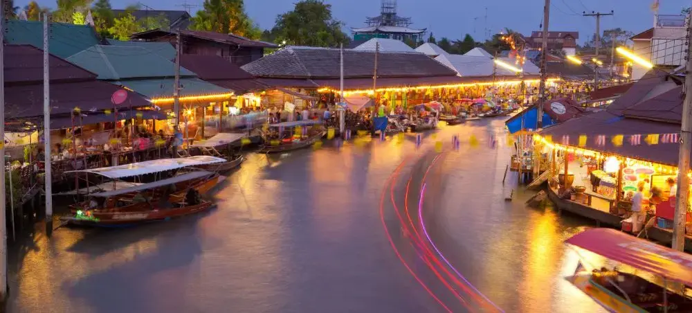 Vibrant floating market in Bangkok at dusk with illuminated vendor boats and light trails on the water