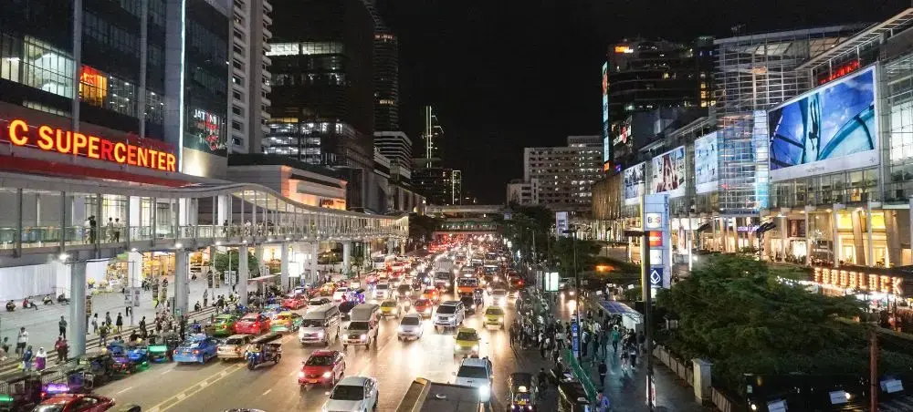 Bustling Bangkok street at night with heavy traffic, illuminated shopping centers and skyscrapers
