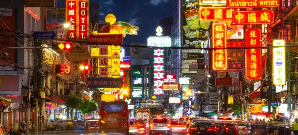 Bustling Bangkok street at night with illuminated Chinese signs and heavy traffic showcasing urban energy