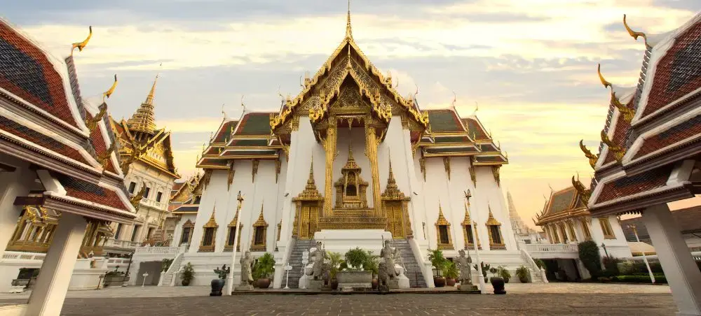 Ornate Thai temple complex with golden spires and white facades in Bangkok's historic district at sunset
