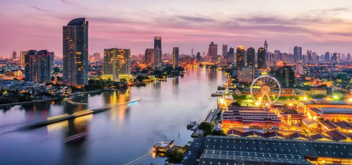 Bangkok skyline at sunset with illuminated skyscrapers reflecting on Chao Phraya River and ferris wheel