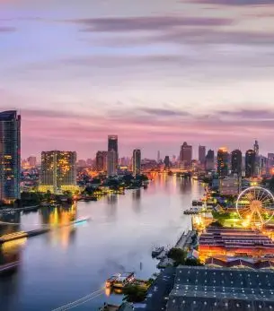 Bangkok skyline at sunset with illuminated skyscrapers reflecting on Chao Phraya River waters