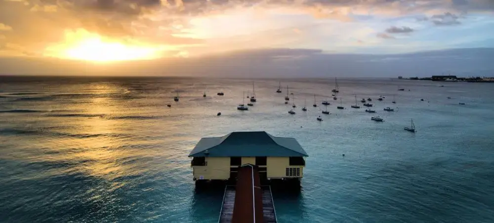 Sunset over Barbados harbor with luxury yachts anchored in turquoise waters and waterfront pier extending into bay